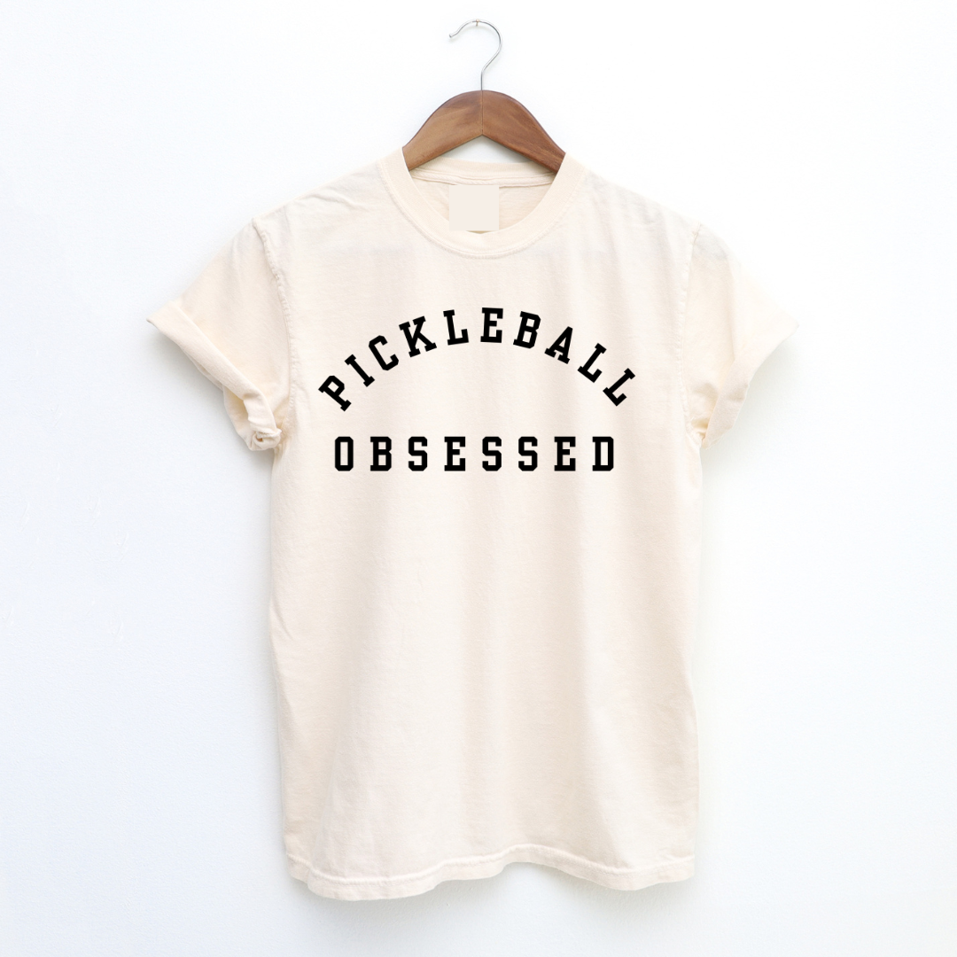 Show your pickleball passion with our Pickleball Obsessed tee! Crafted with impeccable quality. Classic colors.  This tee runs true to size but size up for that effortlessly relaxed fit. Perfect for dominating the courts or adding a dash of pickleball flair to your everyday style. Get ready for your new favorite tee that screams obsession, comfort, and unmistakable pickleball pride!